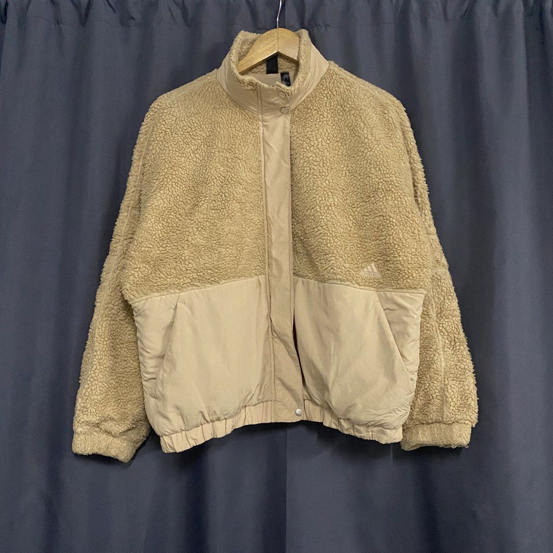 Adidas Beige Sherpa Fleece Jacket (Category: Coats, Jackets and Outerwear) located in Santa Maria. Submitted by saintarchive316 (Listing ID 1467835697, Image 2). Description: - Brand: Adidas - Material: Fluffy sherpa fleece with smooth nylon lower panels - Color: Beige with distinctive brown stripe - Details: High neck collar, zipper with snap-button closure, and side pockets - Branding: 'THREE STRIPES' lettering and logo across the back - Condit