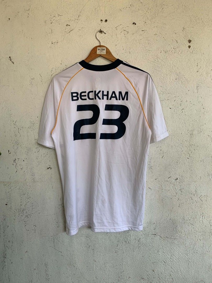 Adidas LA Galaxy Beckham 23 Jersey (Category: Activewear) located in Manila. Submitted by louiseluch69680 (Listing ID 1467654652, Image 2). Description: - Item: LA Galaxy Home Jersey - Player: David Beckham #23 - Color: White with navy blue stripes and yellow piping - Features: Bold vertical 'GALAXY' lettering on the front, Adidas logo, and team crest - Details: Dark blue ribbed collar and cuffs; inner tag shows natural fading from wash and wear 