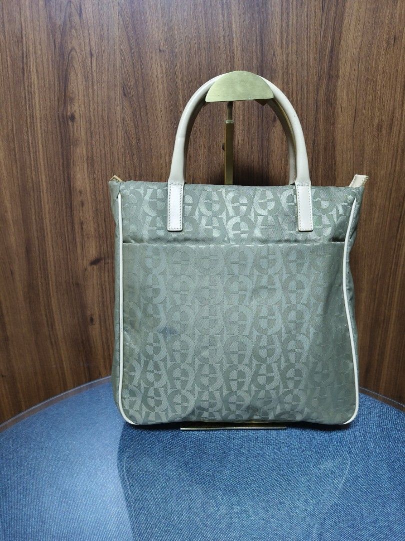 Aigner Vintage Monogram Classic Tote Bag (Category: Tote Bags) located in Baguio. Submitted by PreiLoveMaria (Listing ID 1467761828, Image 2). Description: Aigner tote bag featuring the brand's signature monogram/logo pattern across a durable olive/khaki-toned fabric body, complemented by light beige/cream leather trim and dual top handles. ​Branded with the iconic Aigner logo hardware on the interior leather patch, which also reads "MADE IN ITAL