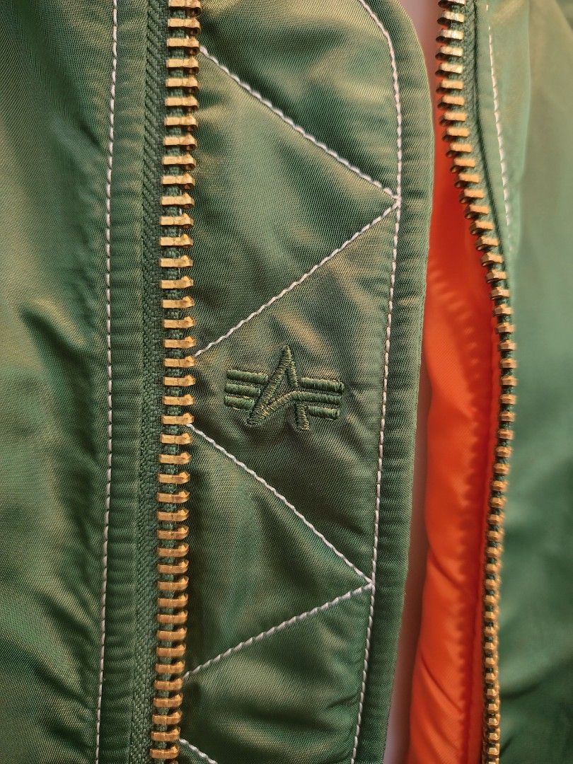 Alpha Industries Green Hooded Bomber Jacket (Category: Coats, Jackets and Outerwear) located in La Trinidad. Submitted by padasem_kadi (Listing ID 1467641646, Image 2). Description: - Brand: Alpha Industries - Color: Sage green with signature bright orange lining - Features: Attached green hood, gold-toned metal zippers, and utility pocket on left sleeve - Details: Quilted inner placket with embroidered logo and contrast white stitching - Fit & C