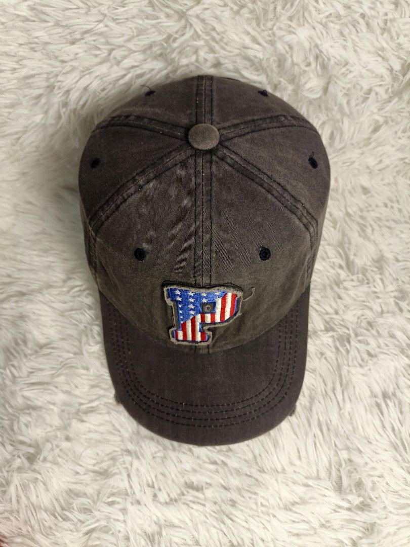 Authentic Pony Dark Grey Baseball Cap With American Flag P Patch (Category: Caps & Hats) located in Imus. Submitted by grindhouse.thriftshop (Listing ID 1467737384, Image 2). Description: - Color: Dark grey with a trendy distressed look - Design: Embroidered 'P' patch with USA flag fill on the front - Build: Classic 6-panel structure with top button and breathable eyelets - Brim: Curved brim with stylish intentional fraying along the edge - Style