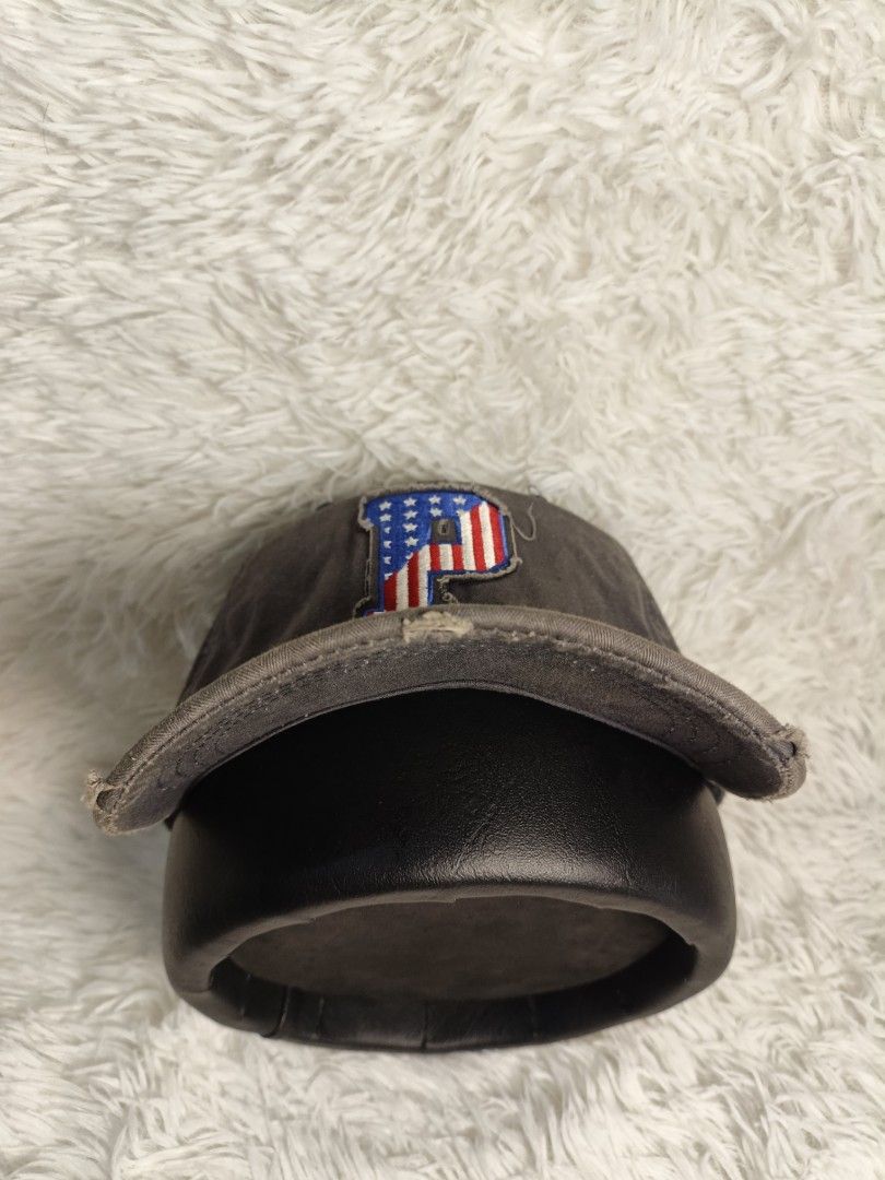 Authentic Pony Dark Grey Baseball Cap With American Flag P Patch (Category: Caps & Hats) located in Imus. Submitted by grindhouse.thriftshop (Listing ID 1467737384, Image 3). Description: - Color: Dark grey with a trendy distressed look - Design: Embroidered 'P' patch with USA flag fill on the front - Build: Classic 6-panel structure with top button and breathable eyelets - Brim: Curved brim with stylish intentional fraying along the edge - Style