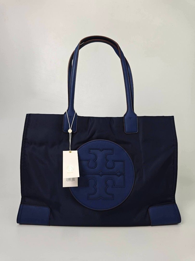 Authentic Tory Burch Ella Nylon Tote Bag Blue (Category: Tote Bags) located in Quezon City. Submitted by hollowwillow (Listing ID 1467616203, Image 1). Description: - Authentic Tory Burch Ella tote in classic Navy Blue - Brand new - Lightweight, durable nylon material with matching handles and bottom corner patches - Features iconic large circular logo stamped on the front - Roomy fabric-lined interior equipped with a secure zip pocket and slip c