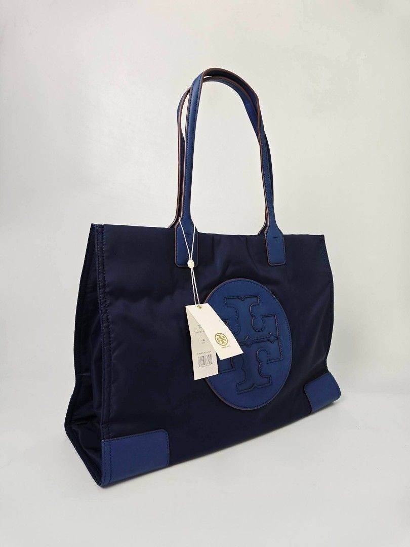 Authentic Tory Burch Ella Nylon Tote Bag Blue (Category: Tote Bags) located in Quezon City. Submitted by hollowwillow (Listing ID 1467616203, Image 2). Description: - Authentic Tory Burch Ella tote in classic Navy Blue - Brand new - Lightweight, durable nylon material with matching handles and bottom corner patches - Features iconic large circular logo stamped on the front - Roomy fabric-lined interior equipped with a secure zip pocket and slip c