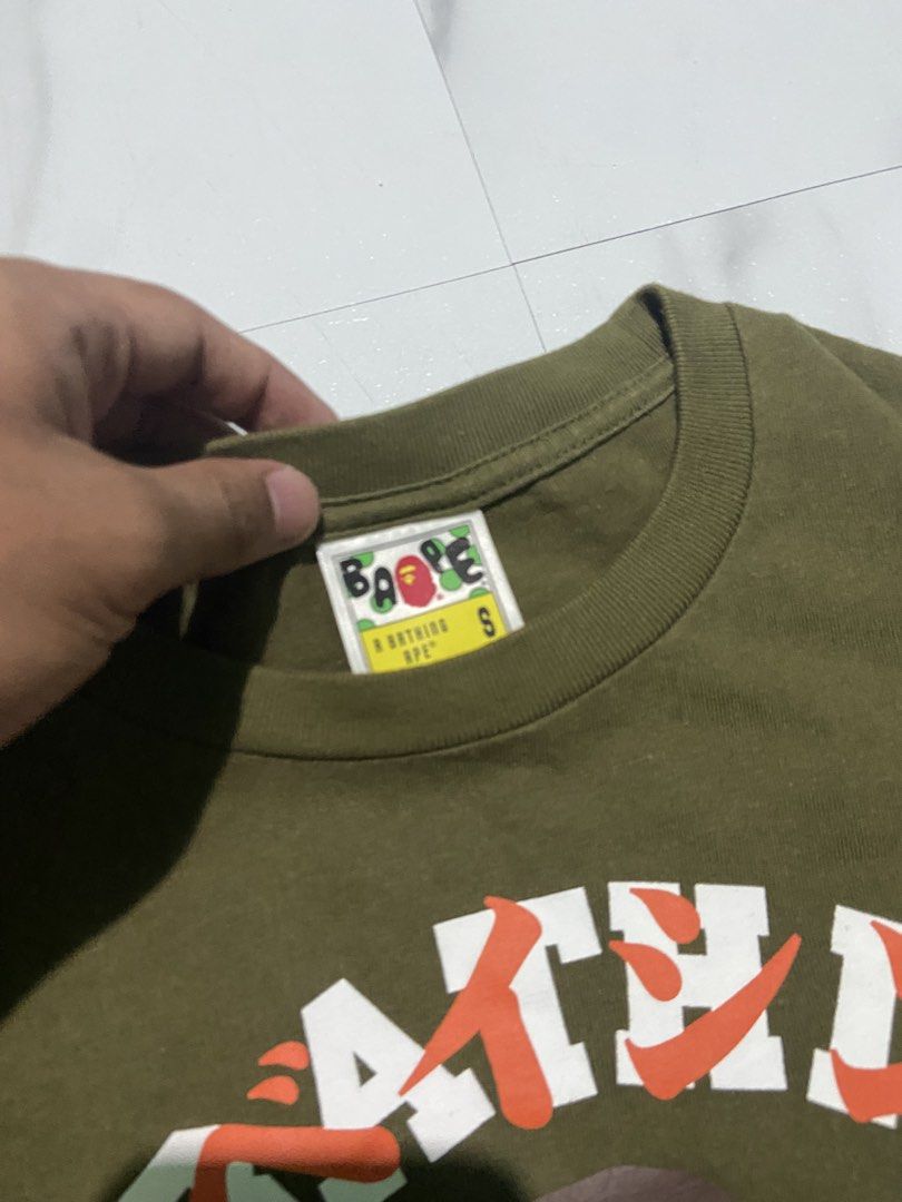BAPE A Bathing Ape Green Graphic Tee Size S (Category: Tshirts & Polo Shirts ) located in Quezon City. Submitted by johncen (Listing ID 1467725876, Image 3). Description: - Brand: BAPE - Color: Olive green - Size: Small (collar tag verified) - Design: Classic ape head graphic with bold white and orange text - Details: Embroidered ape patch on the sleeve - Material: Heavyweight cotton - Condition: Clean fabric with crisp, high-quality print.