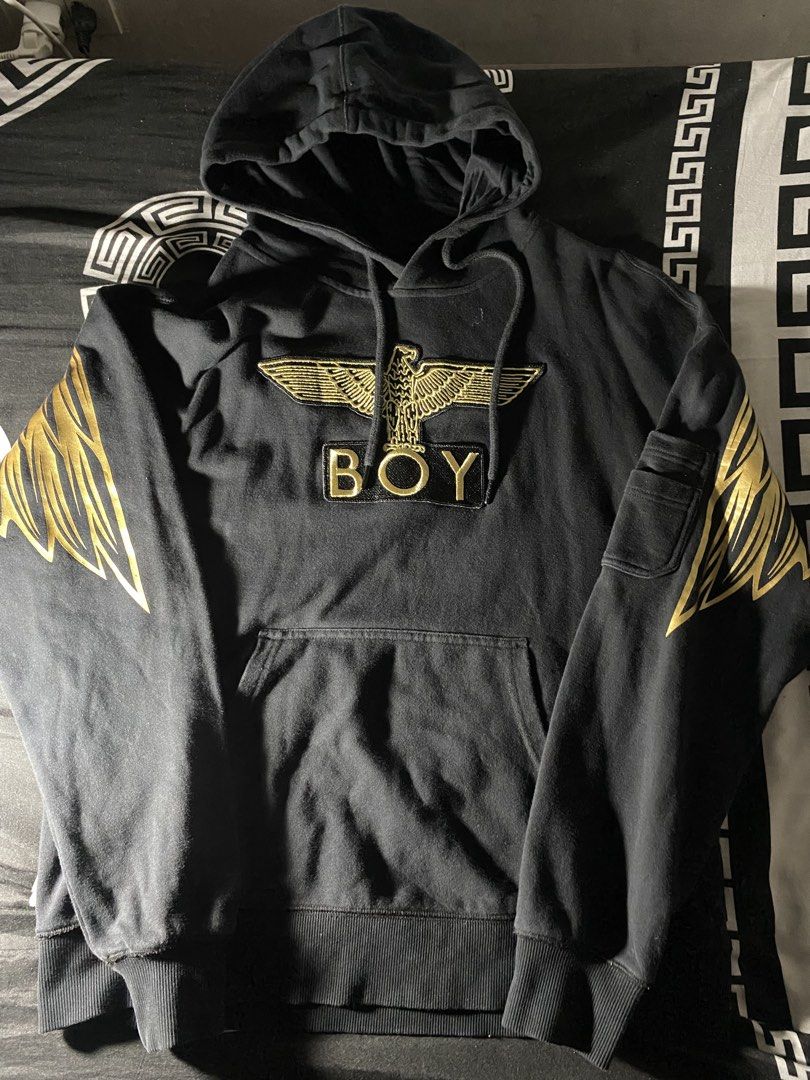 Boy London Black Gold Eagle Wings Pullover Hoodie (Category: Coats, Jackets and Outerwear) located in Caloocan City. Submitted by drip_archive (Listing ID 1467826868, Image 1). Description: - Brand: Boy London - Color: Black with metallic gold foil accents - Design: Large gold wings and chain graphic on back, matching sleeve prints, and embroidered front eagle patch - Features: Front kangaroo pocket, extra utility pocket on left sleeve, and adjus