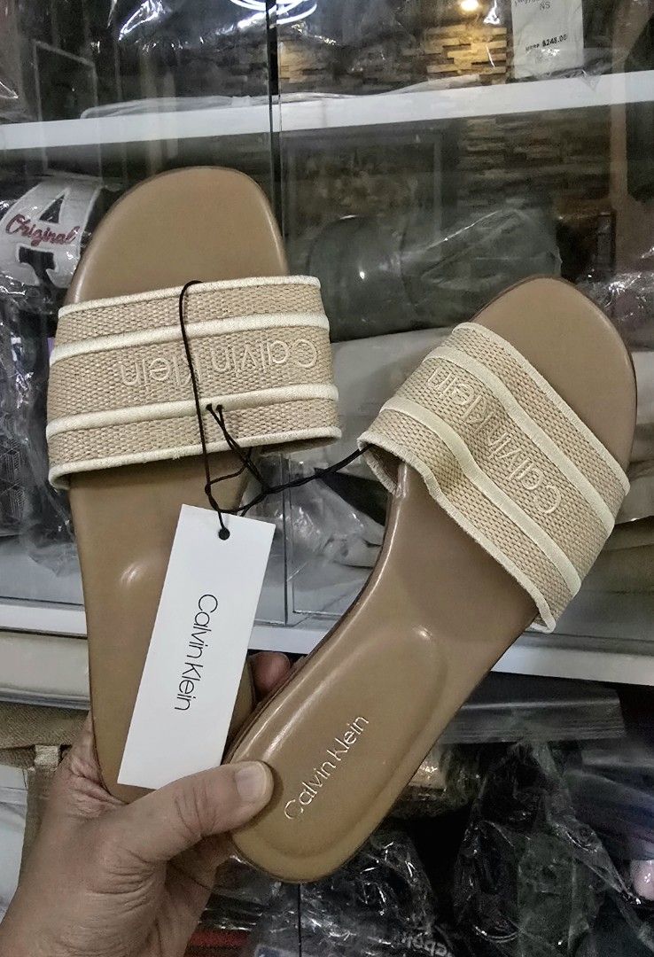 Calvin Klein Beige Slide Sandals (Category: Flats & Sandals) located in Quezon City. Submitted by momof3_11 (Listing ID 1467758071, Image 1). Description: - Brand: Calvin Klein - Color: Beige with brown footbed - Condition: Brand new, never worn, with original tag attached - Design: Woven strap with embroidered brand name - Comfort: Flat sole with a cushioned footbed - Perfect for casual everyday wear.