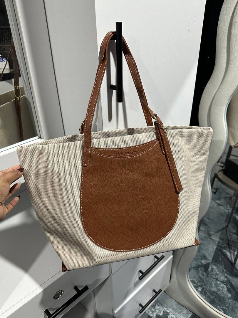 Canvas and Leather Tote Bag Brown (Category: Luxury Bags & Wallets) located in Las Pinas. Submitted by ladyattire (Listing ID 1467638752, Image 1). Description: - Brand: Longchamp - Material: Beige canvas with brown textured leather trim - Straps: Dual shoulder straps with gold-tone buckle hardware and logo branding - Exterior: Front rounded leather pocket with white contrast stitching and debossed Longchamp text - Interior: Spacious fabric-lined