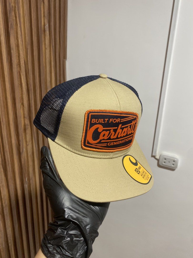 Carinhart AH6928-M Built For Generations Trucker Cap (Category: Caps & Hats) located in Caloocan City. Submitted by heatedcaps4425 (Listing ID 1467803833, Image 2). Description: - Brand: Carhartt (Model: AH6928-M) - Condition: Brand new with tags, never worn - Color: Tan front panels with dark navy mesh back - Design: Orange and navy embroidered 'Built For Generations' patch logo - Brim: Flat brim with original Force sticker attached - Material: 