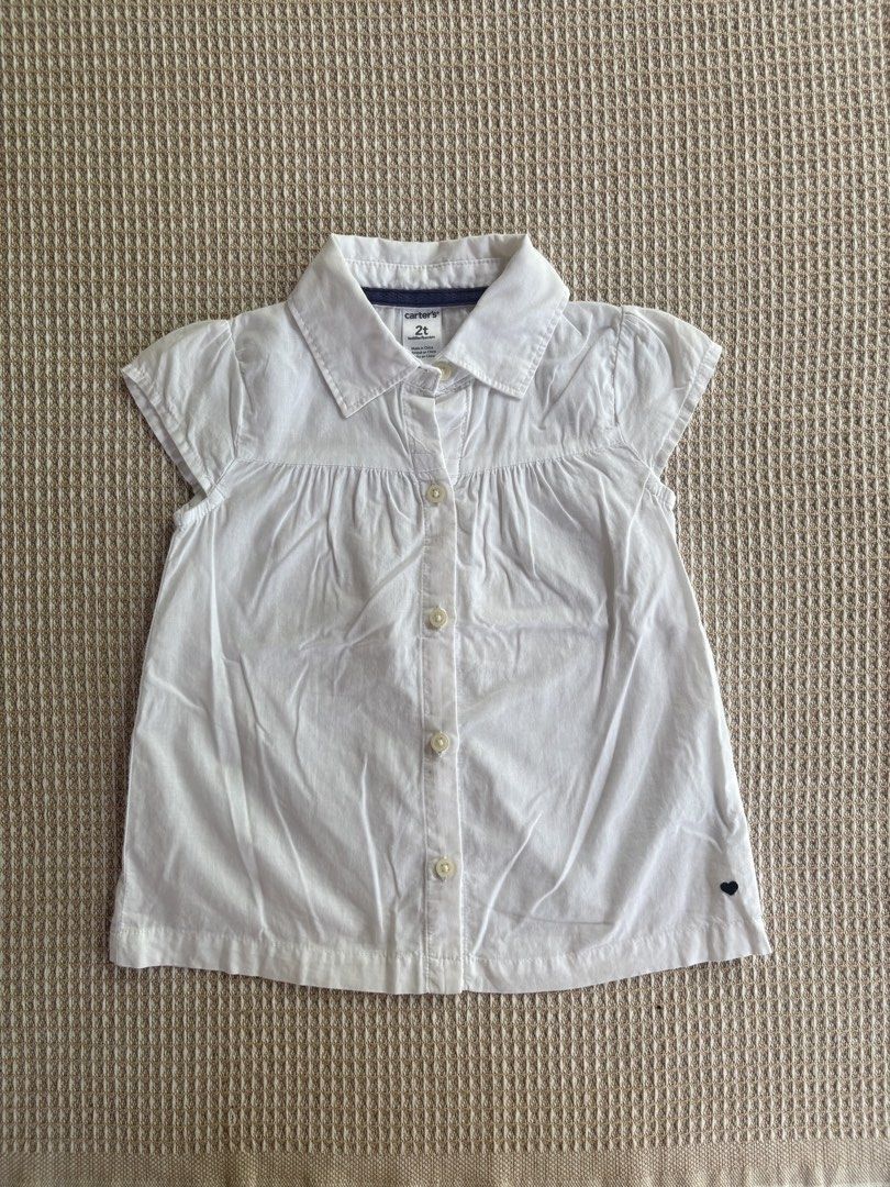 Carter's White Button-Down Shirt Size 2T (Category: Babies & Kids Fashion) located in San Juan, La Union. Submitted by jcmami_ (Listing ID 1467711628, Image 1). Description: - Brand: Carter's - Size: 2T - Color: Clean White - Style: Short cap sleeves, collared neckline, and front button closure - Details: Charming pleated front with a small dark heart graphic near the bottom hem - Condition: Great, simple everyday wear for toddler girls.