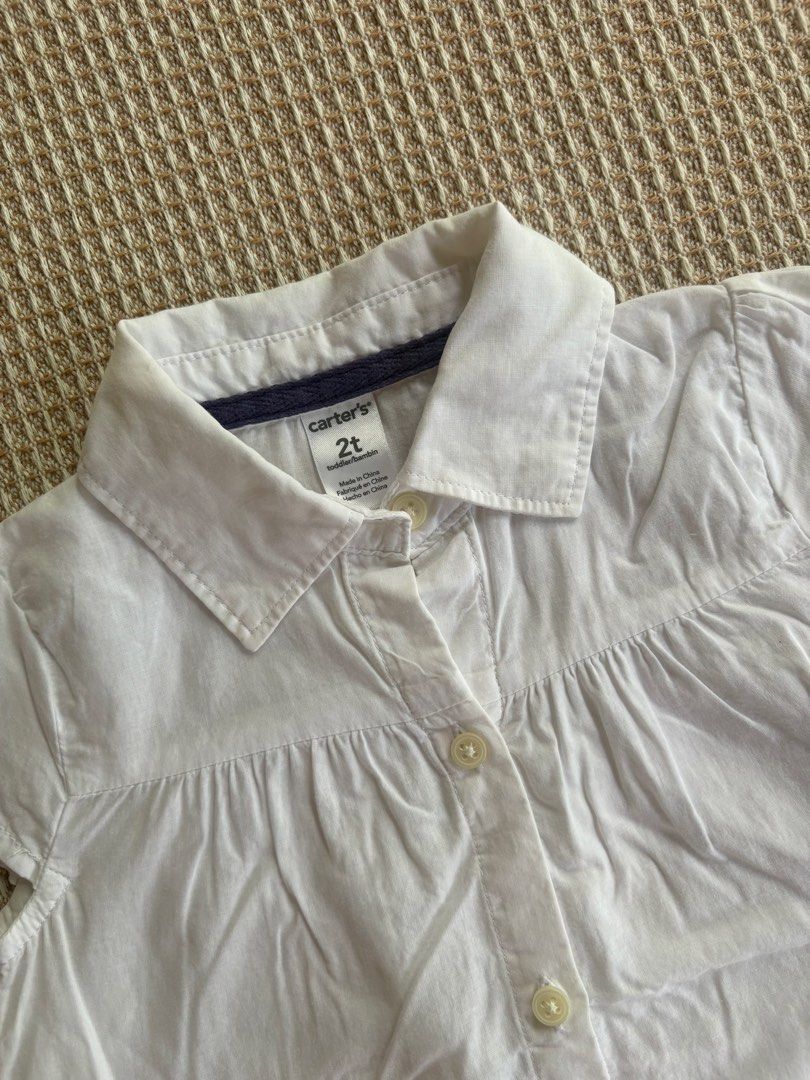 Carter's White Button-Down Shirt Size 2T (Category: Babies & Kids Fashion) located in San Juan, La Union. Submitted by jcmami_ (Listing ID 1467711628, Image 2). Description: - Brand: Carter's - Size: 2T - Color: Clean White - Style: Short cap sleeves, collared neckline, and front button closure - Details: Charming pleated front with a small dark heart graphic near the bottom hem - Condition: Great, simple everyday wear for toddler girls.