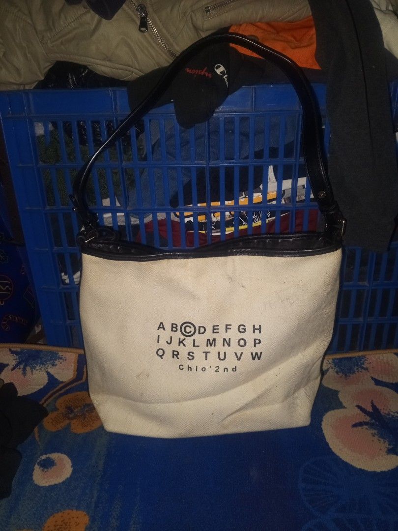 Chio 2nd (Category: Shoulder Bags) located in Magalang. Submitted by zeiansoria64090 (Listing ID 1467675995, Image 1). Description: - Brand/Model: Chio 2nd shoulder bag - Color: Cream canvas with black leather trim and straps - Design: Unique alphabet typography print on the front exterior - Interior: Fully lined with black fabric, featuring an inner zip pocket, gold-tone brand plate, and slip pockets - Closure: Secure magnetic snap closure - Con