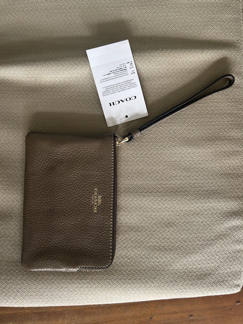 Coach Brown Leather Wristlet (Category: Purses & Pouches) located in Pasig City. Submitted by piayayaya511 (Listing ID 1467607985, Image 1). Description: - Brand: Coach - Material: Premium brown pebbled leather - Hardware: Elegant gold-tone - Features: Secure zip-top closure, attached wrist strap, and fabric-lined interior with two card slots - Condition: Brand new with original tag still attached - Details: Smooth zipper pull and clean, high-qua