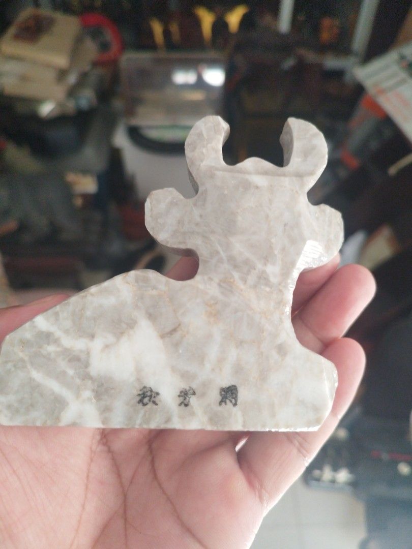 Cow curved stone (Category: Vintage Collectibles) located in San Rafael. Submitted by jflshoppe1989 (Listing ID 1467671454, Image 2). Description: The image shows a hand-carved stone figurine of a resting cow or calf, featuring a light grey and white marbled stone body, painted dark horns and ears, and a red-and-white patterned collar with a yellow ring detail..