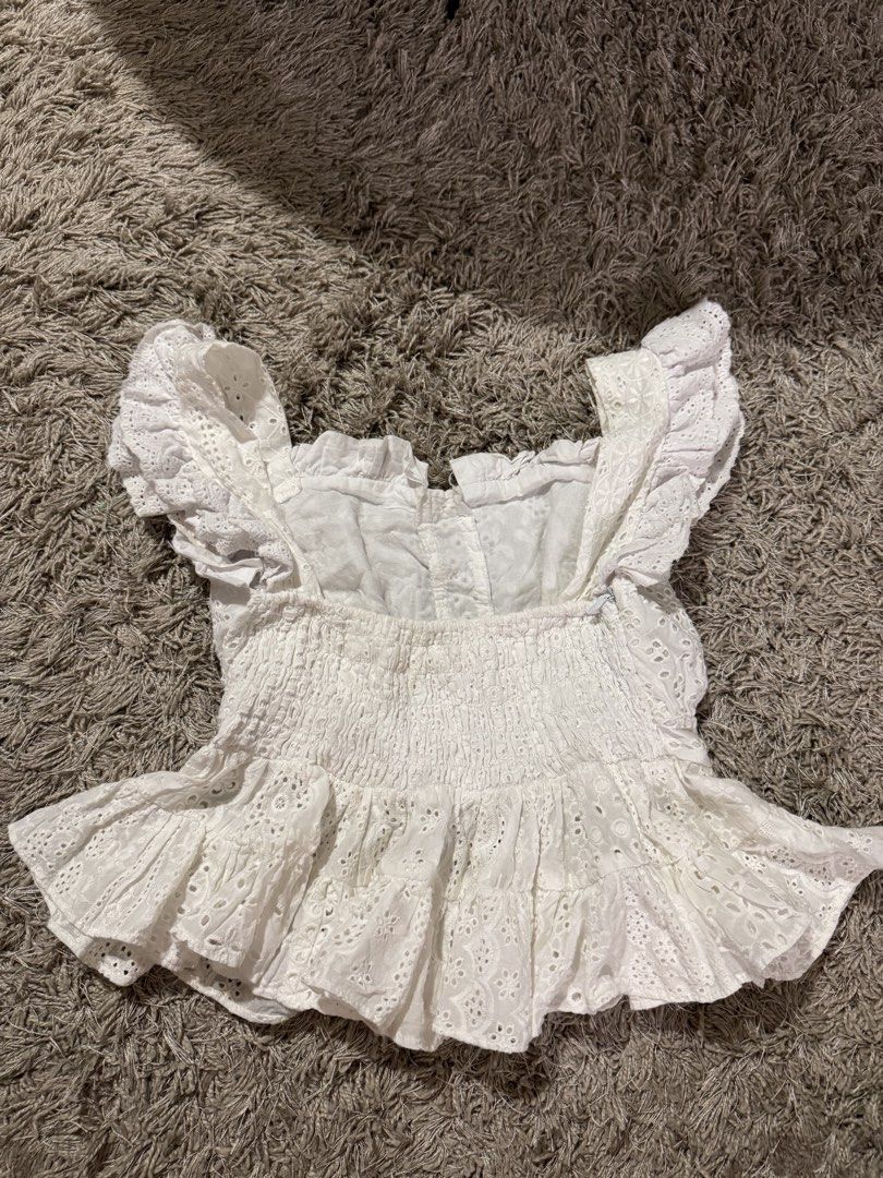 Dreamland White Eyelet Ruffle Crop Top Size S (Category: Blouses) located in Caloocan City. Submitted by newcrystal_3b43ba (Listing ID 1467738539, Image 2). Description: - Brand: Dreamland - Size: Small (tag attached) - Color: Clean white with intricate floral eyelet cutouts - Design: Square neckline with ruffle shoulder straps - Closure: Button-front with a stretchy smocked back panel - Detail: Layered ruffle hem.