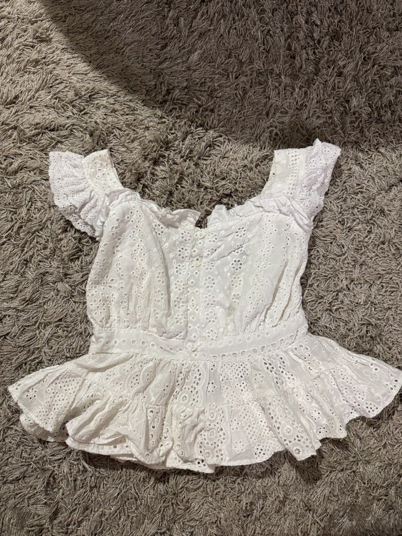 Dreamland White Eyelet Ruffle Crop Top Size S (Category: Blouses) located in Caloocan City. Submitted by newcrystal_3b43ba (Listing ID 1467738539, Image 1). Description: - Brand: Dreamland - Size: Small (tag attached) - Color: Clean white with intricate floral eyelet cutouts - Design: Square neckline with ruffle shoulder straps - Closure: Button-front with a stretchy smocked back panel - Detail: Layered ruffle hem.