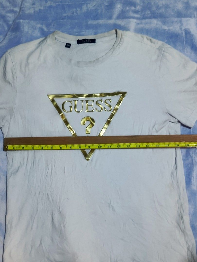 GUESS Gold Triangle Logo White T-Shirt (Category: Shirts) located in City of Isabela. Submitted by warmbird.d06e6f (Listing ID 1467637529, Image 3). Description: - Authentic Guess t-shirt in classic white - Features a stylish gold foil triangle logo on the chest - Size & Fit: Regular fit, crew neck, short sleeves - Dimensions: ~19" chest width, ~26" length - Verified authentic with interior sizing/care tags and Korean authorized authentication ta