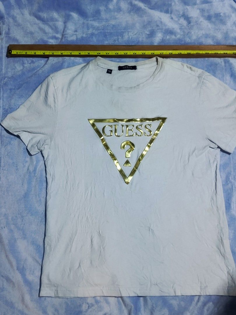 GUESS Gold Triangle Logo White T-Shirt (Category: Shirts) located in City of Isabela. Submitted by warmbird.d06e6f (Listing ID 1467637529, Image 1). Description: - Authentic Guess t-shirt in classic white - Features a stylish gold foil triangle logo on the chest - Size & Fit: Regular fit, crew neck, short sleeves - Dimensions: ~19" chest width, ~26" length - Verified authentic with interior sizing/care tags and Korean authorized authentication ta
