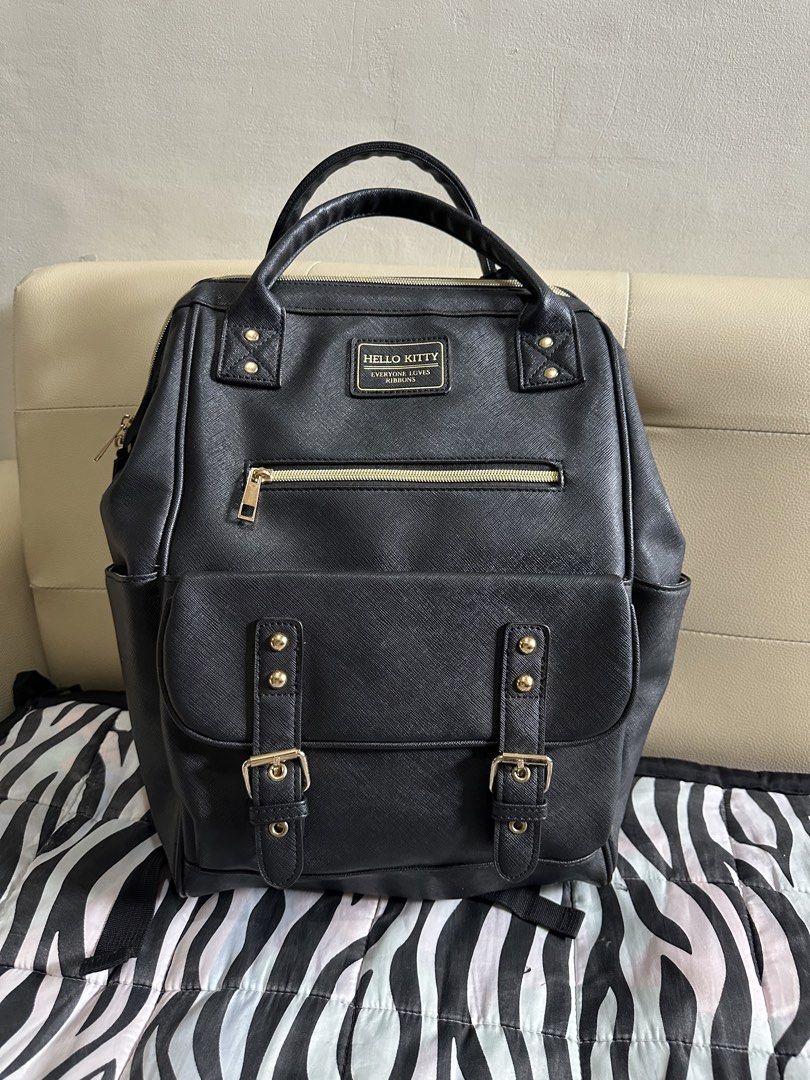 Hello Kitty Black Saffiano Leather Backpack Sanrio (Category: Backpacks) located in Imus. Submitted by ana1990_ (Listing ID 1467734182, Image 1). Description: - Style: Black faux leather Kitty backpack with gold-tone hardware - Texture: Saffiano texture all over with a sturdy build - Compartments: Front flap pocket, zip pocket, and multiple inner pockets - Comfort: Top handles and adjustable shoulder straps with breathable mesh backing - Interior