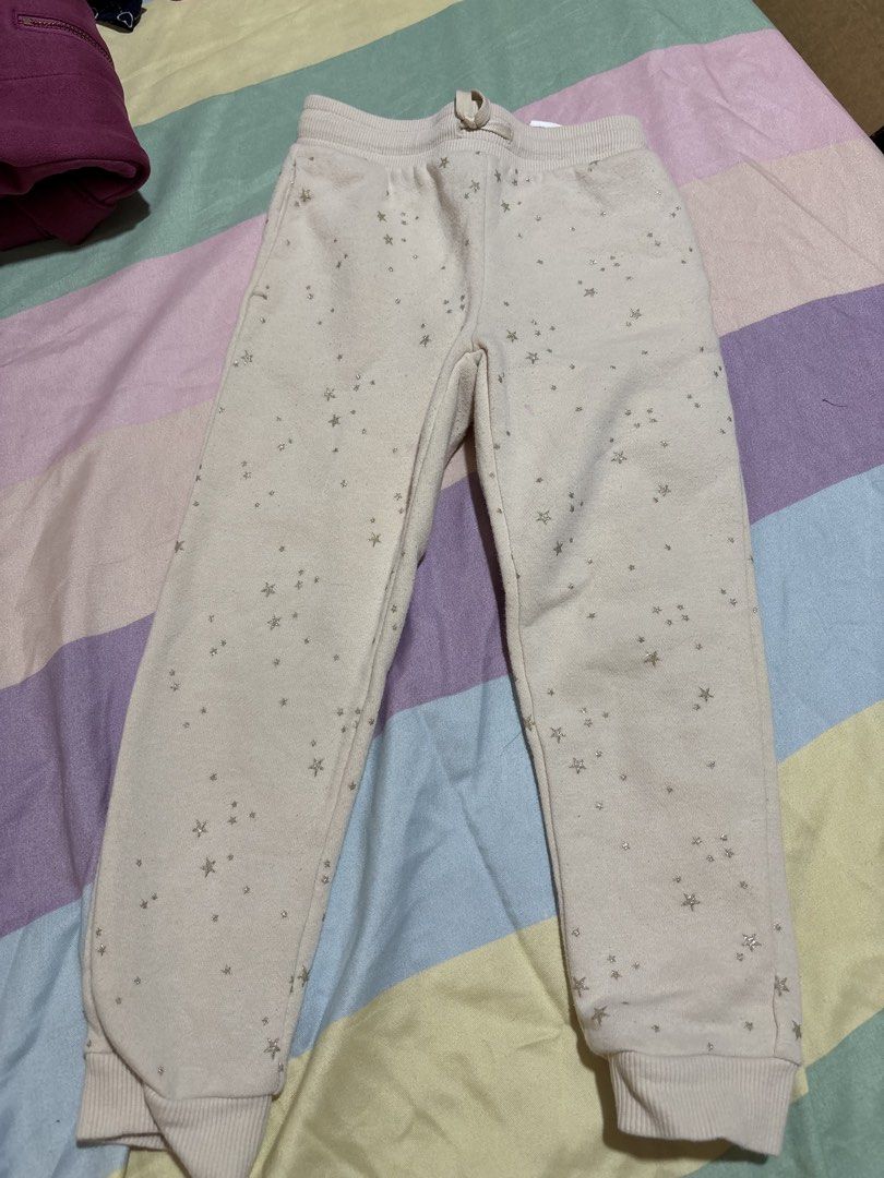 H&M Star Print Sweatpants Joggers (Category: Babies & Kids Fashion) located in Manila. Submitted by wardrobeinmnl (Listing ID 1467690981, Image 1). Description: - Brand/Item: H&M Beige Sweatpants with Sparkly Gold Stars - Size: EUR 104, US 4T, 3-4 Years - Material: Comfortable cotton blend with soft fleece lining - Features: Elastic waistband, adjustable drawstring, and ribbed ankle cuffs - Condition: Pre-loved with a slight pink stain near the f