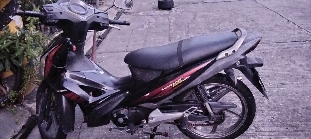 Honda Wave 125R Motorcycle (Category: Motorbikes for Sale) located in Mandaluyong City. Submitted by dhaliwal086 (Listing ID 1467709720, Image 1). Description: Honda Wave 125R motorcycle in black and red. Mileage reads 52631 kilometers. Fuel gauge sits near empty. Chain drive system with stock exhaust pipe. Standard step bars and grab handle attached. License plate reads P8964Y. Engine starts and runs fine. Normal wear from daily commuting..