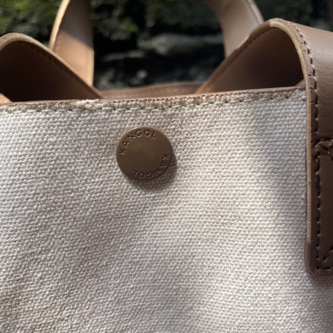 Kangol Tiny Canvas Tote Bag KNEB-TB3350 (Category: Tote Bags) located in Valenzuela. Submitted by mikayruu (Listing ID 1467642987, Image 3). Description: - Brand: Kangol - Style: Canvas Tote (Style Code: KNEB-TB3350) - Color: Ivory with brown leather-look trim and handles - Closure: Top snap button - Strap: Includes matching detachable shoulder strap - Interior: Features an official Kangol tag and slip pocket - Condition: Clean interior lining wi