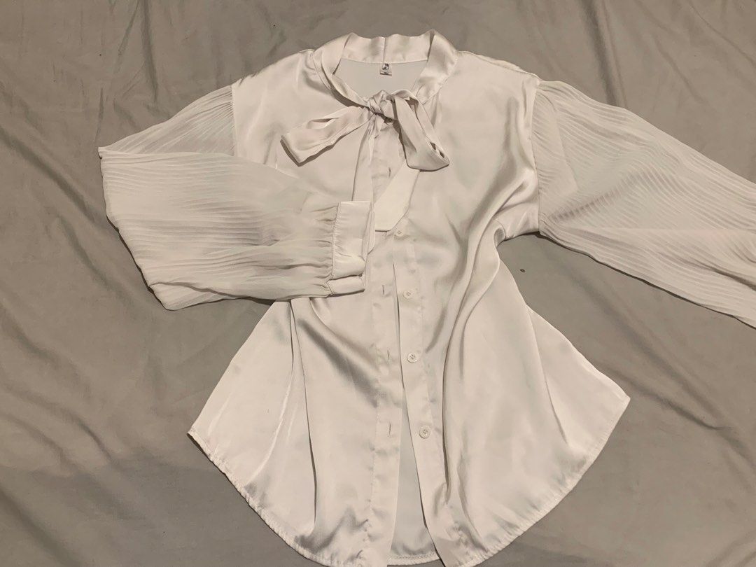 Korean Style Blouse (Category: Blouses) located in Manila. Submitted by coquettecore (Listing ID 1467773197, Image 1). Description: Gorgeous white satin blouse featuring a chic tie-neck and elegant pleated sleeves. Smooth, shiny fabric with a button-up front and rounded hem. Korean inspired blouse. Size:Medium-Large Color: Off White / silver grayish hue (not cream) Sleeves are mesh fabric .