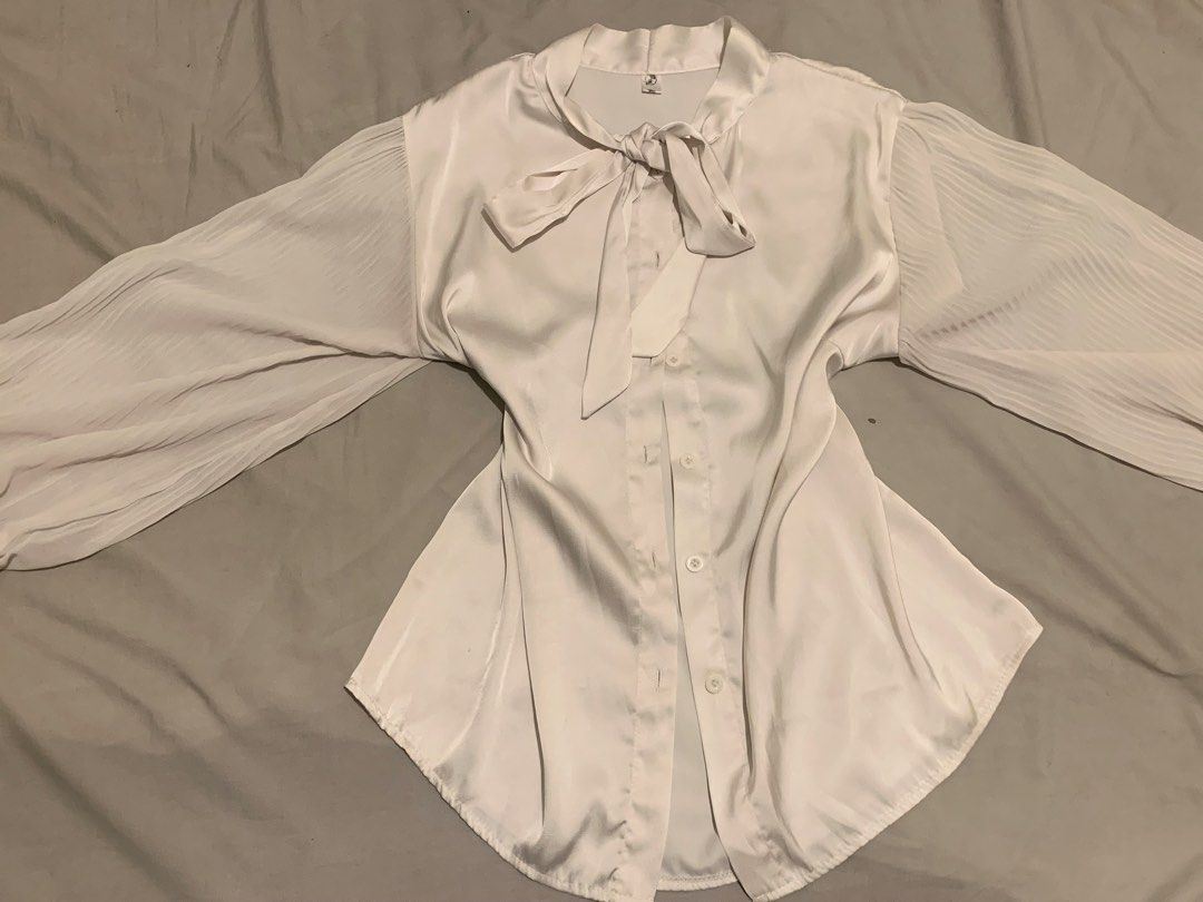 Korean Style Blouse (Category: Blouses) located in Manila. Submitted by coquettecore (Listing ID 1467773197, Image 2). Description: Gorgeous white satin blouse featuring a chic tie-neck and elegant pleated sleeves. Smooth, shiny fabric with a button-up front and rounded hem. Korean inspired blouse. Size:Medium-Large Color: Off White / silver grayish hue (not cream) Sleeves are mesh fabric .