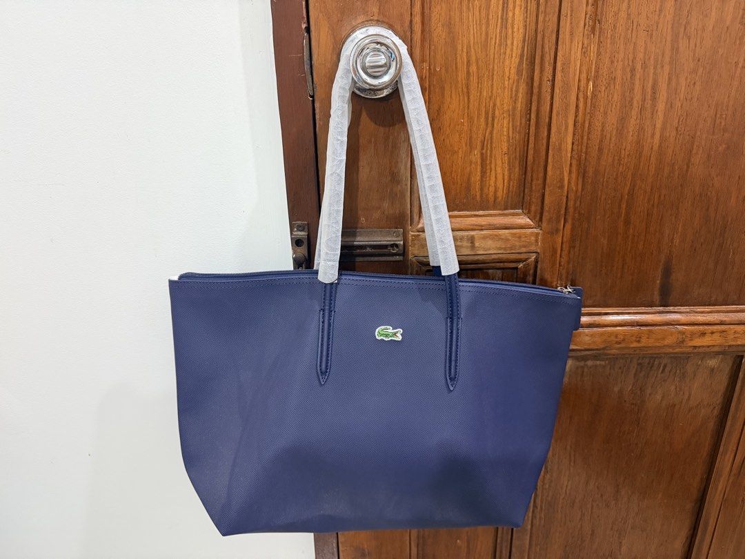 Lacoste Navy Blue Tote Bag (Category: Tote Bags) located in Kalibo. Submitted by goodfinds.club (Listing ID 1467766377, Image 1). Description: - Authentic navy blue Lacoste tote bag - Brand new with handles still in original protective foam packaging - Structured, textured material with a secure zippered top - Features the signature green crocodile logo on the front - Spacious interior, ideal for daily essentials and everyday use.