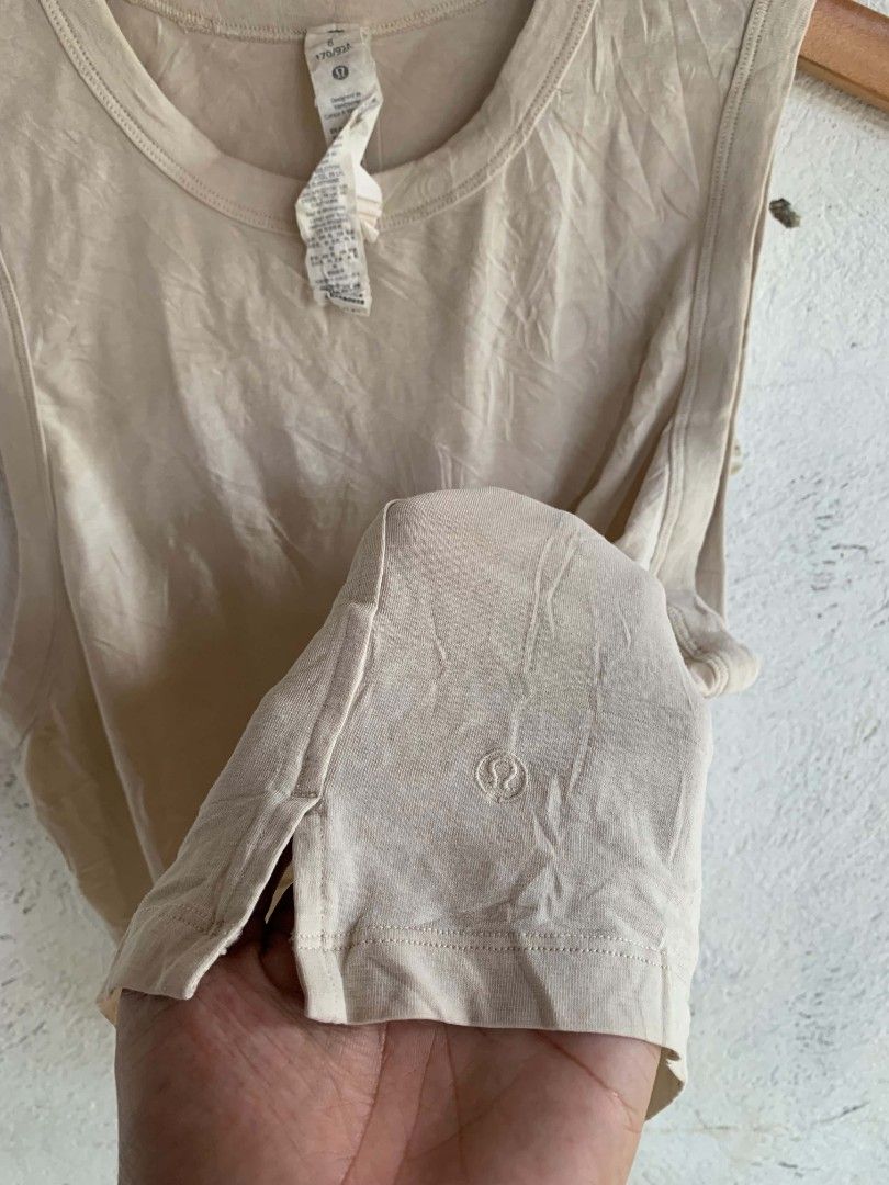 Lululemon Beige Tank Top Size 8 (Category: Sleeveless) located in Manila. Submitted by louiseluch69680 (Listing ID 1467644361, Image 3). Description: - Brand: Lululemon - Style: Sleeveless tank top with round neckline and side slit hem - Color: Neutral beige - Size: 8 (dimes 18x19.5) - Material: Lightweight cotton, lyocell, and linen blend - Details: Subtle embossed Lululemon logo near the bottom corner - Condition: Excellent, versatile for worko