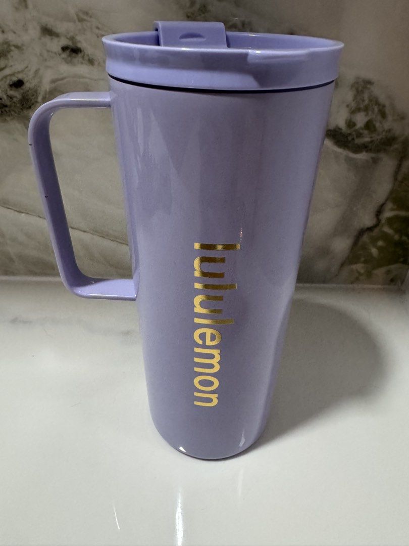 Lululemon Lavender Travel Mug with Handle (Category: Water Bottles & Tumblers) located in Manila. Submitted by decluterthings888 (Listing ID 1467740041, Image 2). Description: - Brand: Lululemon - Color: Soft lavender purple with a vertical gold logo - Lid: Secure with a sliding closure mechanism - Features: Convenient side handle for easy sipping - Base: Textured with embossed Lululemon omega logo - Condition: Clean interior and exterior, ready 