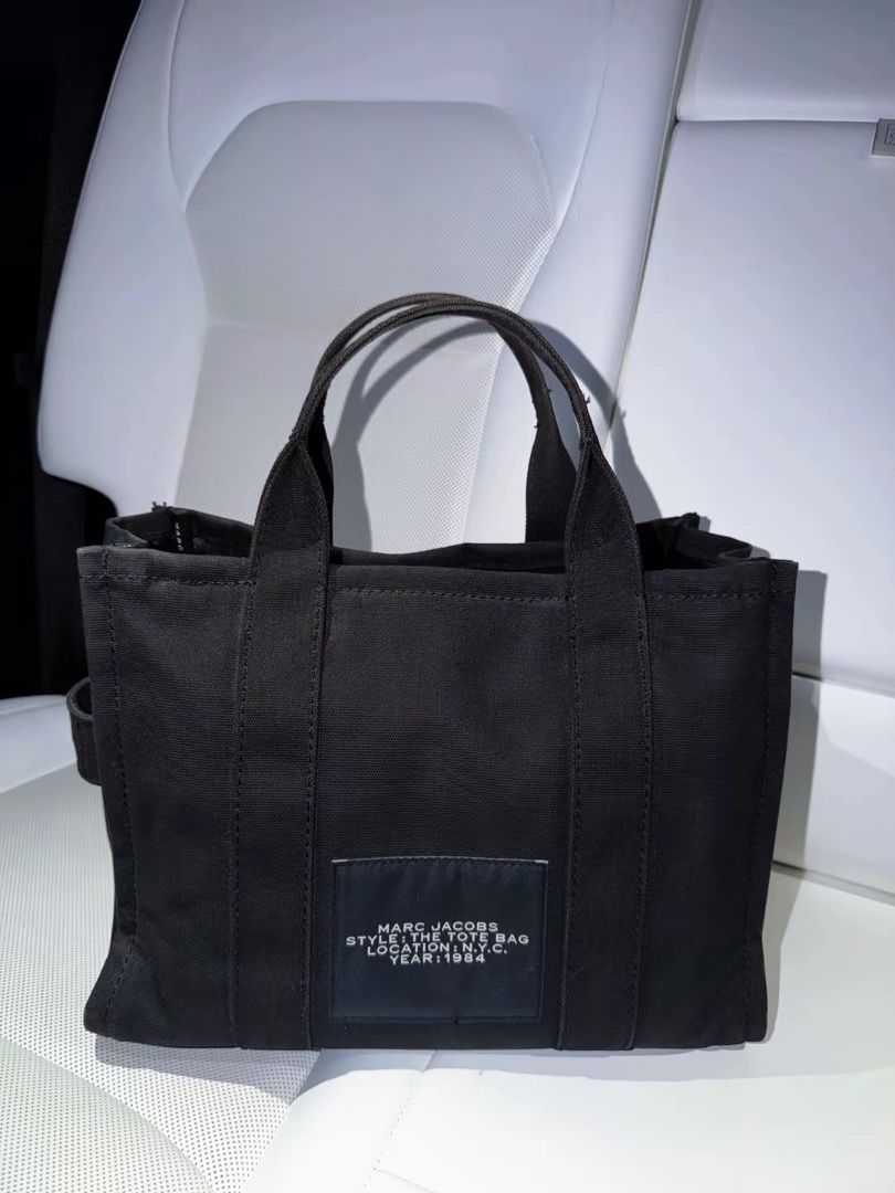Marc Jacobs The Tote Bag Black Canvas (Category: Luxury Bags & Wallets) located in Quezon City. Submitted by mofu1 (Listing ID 1467772200, Image 2). Description: - Brand: Marc Jacobs - Material: Durable black canvas with signature white lettering - Versatile carry: Includes matching top handles and a removable, adjustable shoulder strap - Design: Structured shape with chic side strap details - Back details: Authentic brand patch with style info a