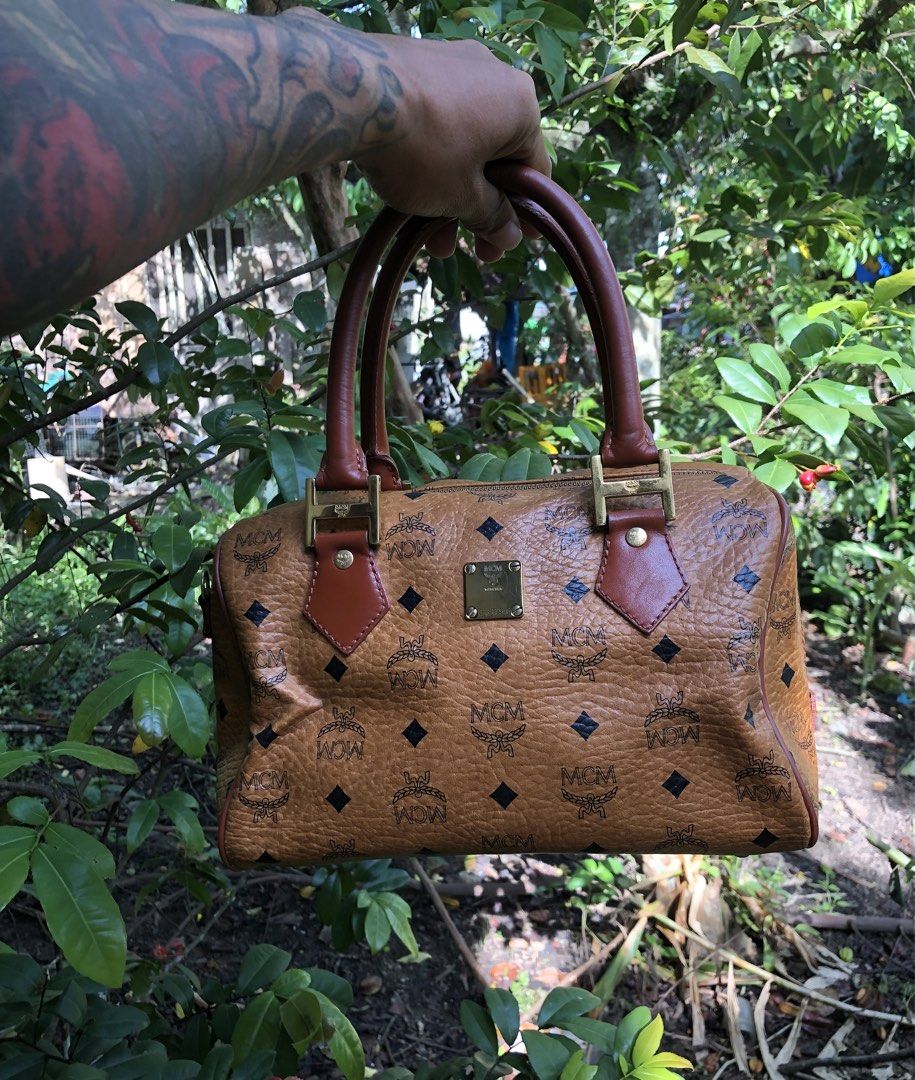 MCM Monogram Leather Boston Bag (Category: Luxury Bags & Wallets) located in Montevista. Submitted by rdthriftshub (Listing ID 1467714326, Image 1). Description: - Iconic MCM Boston bag in classic cognac Visetos monogram leather - Structured design with luxurious gold-tone hardware and brown leather trim - Secure top zip closure with dual top handles for easy carrying - Fabric-lined interior featuring a convenient inner zippered pocket - Compact 