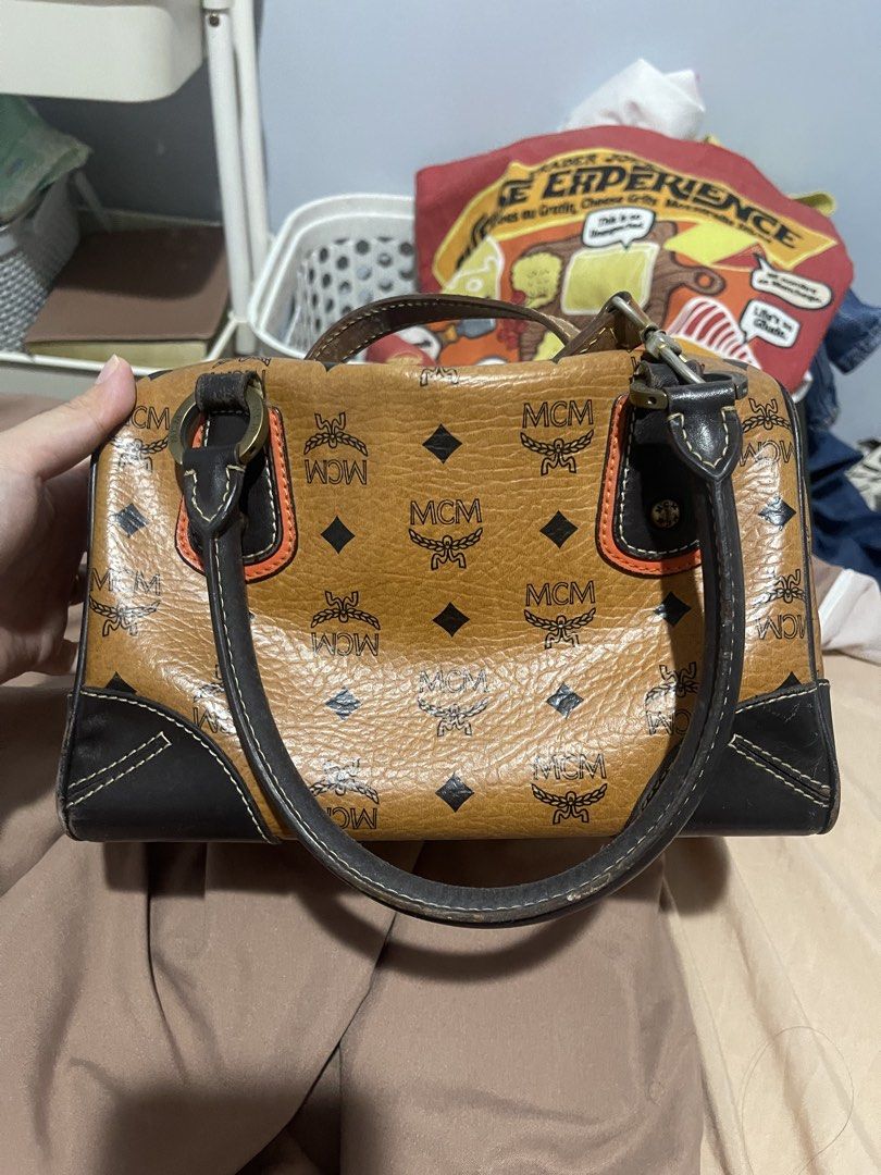 MCM Visetos Monogram Boston Dark Brown (Category: Luxury Bags & Wallets) located in Mabalacat. Submitted by khariz.v.ramirez (Listing ID 1467678125, Image 2). Description: - Authentic classic MCM Boston bag in signature cognac Visetos print - Dark brown leather trim with stylish contrasting orange side stripes - Brass-tone hardware and structured shape with protective bottom studs - Secure top zipper closure with spacious interior for daily essen