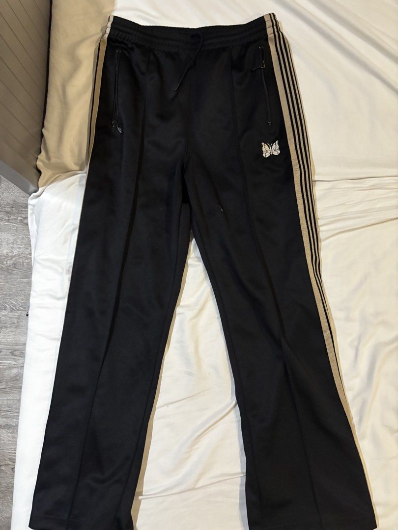 Needles Black Track Pants with Tan Stripes (Category: Joggers) located in Manila. Submitted by zxcvbnm_100 (Listing ID 1467732161, Image 1). Description: - Brand: Needles - Color: Black with tan side stripes - Details: Iconic embroidered butterfly logo on the left hip - Storage: Secure zippered front pockets - Fit: Relaxed fit with an elastic waistband and adjustable drawstring - Material: Smooth, premium polyester fabric - Condition: Excellent /