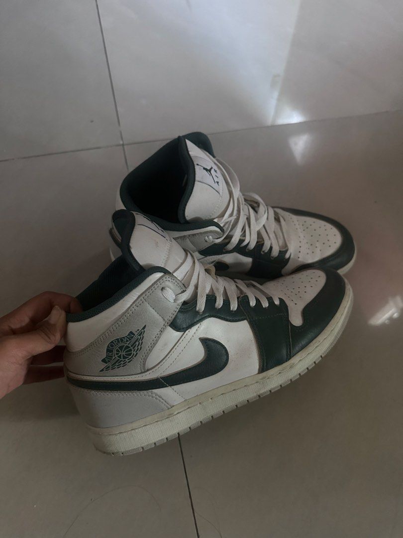Nike Air Jordan 1 Sneakers (Category: Sneakers) located in San Miguel. Submitted by monicakettle (Listing ID 1467663151, Image 2). Description: - Model: Air Jordan 1 Mid - Colorway: White and Dark Navy Green - Design: Classic high-top silhouette with perforated toe box, signature swoosh, Jumpman tongue logo, and stamped Wings logo - Condition: Normal wear on soles and creases on the toe box - Perfect as a solid everyday rotation pair.