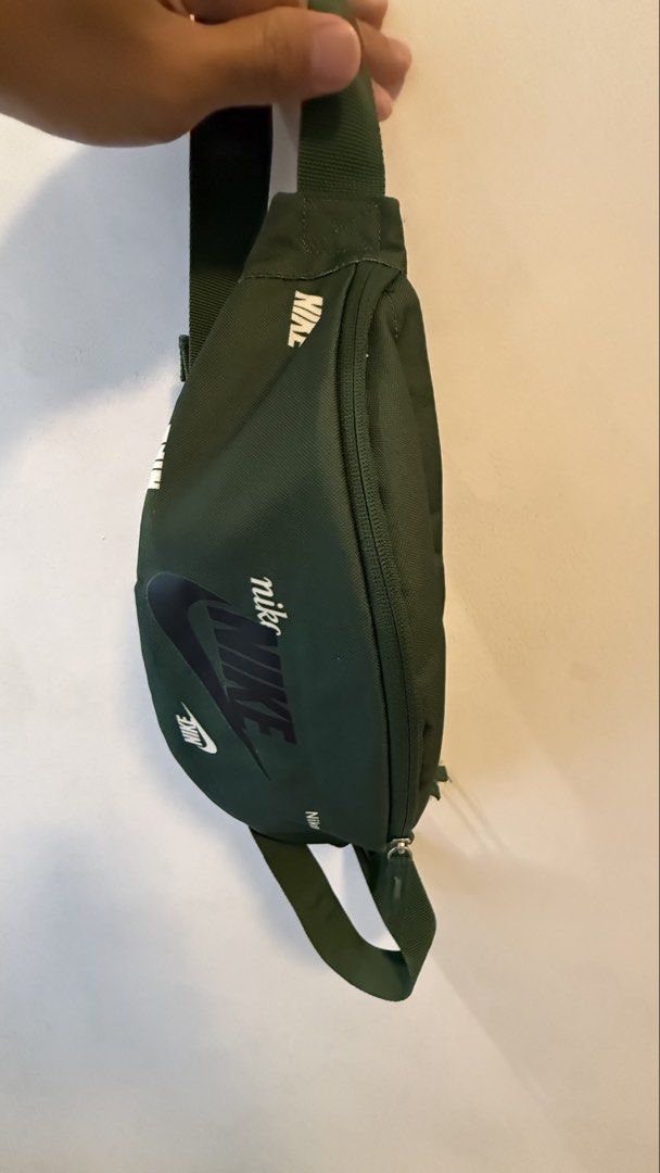 Nike Green Crossbody Bag (Category: Sling Bags) located in Quezon City. Submitted by kobeeeee_12 (Listing ID 1467736304, Image 1). Description: - Brand: Nike - Color: Dark green with white all-over brand text prints - Material: 100% polyester - Closure: Secure zipper - Strap: Adjustable with durable plastic buckle - Interior: Fabric lining with handy mesh pockets - Condition: Clean tag visible inside - Size: Compact and convenient for daily essen