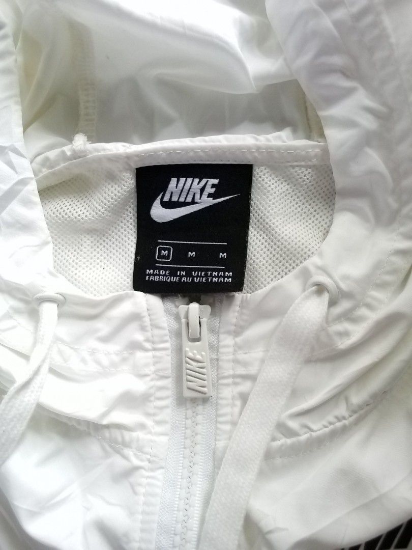 Nike White Windbreaker Jacket Size M (Category: Coats, Jackets and Outerwear) located in Veruela. Submitted by durojaarce23468 (Listing ID 1467653151, Image 3). Description: - Brand: Nike - Style: Windbreaker jacket - Color: White with black chest logo - Size: Medium 21x25 - Style Code: AJ2983-100 - Origin: Made in Vietnam - Features: Full zip closure, hood with adjustable drawstrings, and vented upper back panel with mesh inner lining - Material