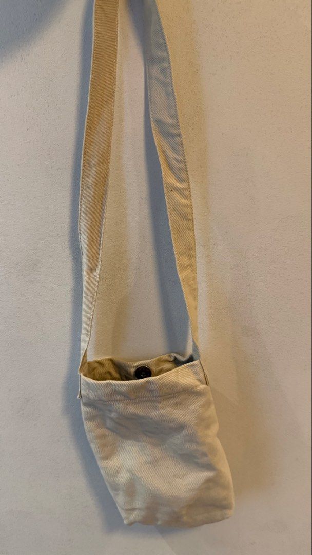 Off-white canvas crossbody bag with magnetic button (Category: Cross-body Bags) located in Quezon City. Submitted by kobeeeee_12 (Listing ID 1467737095, Image 1). Description: - Color: Off-white - Material: Durable canvas - Closure: Secure snap button at the top - Interior: Dark lining - Strap: Simple long strap design - Perfect size for daily essentials (phone, keys, wallet) - Ideal for casual, everyday use.