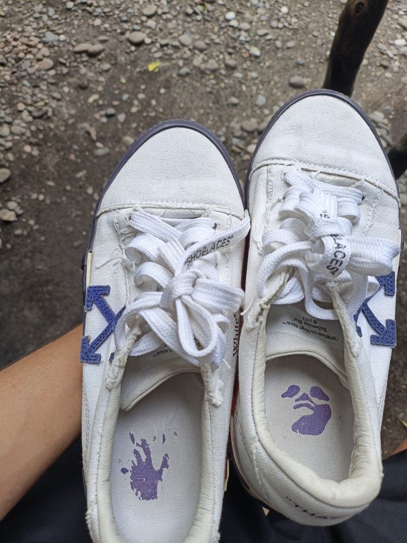 Off-White Vulcanized Low Sneakers White Blue (Category: Sneakers) located in Maasim. Submitted by ukayganda25 (Listing ID 1467656829, Image 3). Description: - Brand: Off-White - Style: Low top sneakers in white canvas with iconic blue arrow details - Design: Vulcanized sole with text on bottom, 'SHOELACES' lettering on laces, and a purple hand graphic on the insoles - Condition: Pre-owned with some visible wear on the canvas and soles - Vibe: Per