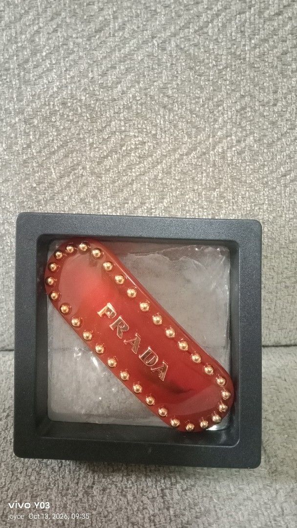 Prada Red Hair Clip with Gold Studs (Category: Hair Accessories) located in Cabuyao City. Submitted by selections888 (Listing ID 1467612809, Image 2). Description: - Brand: Prada - Material: Premium red acetate with gold-tone hardware - Design: Gold-tone metal studs along the border with raised gold Prada lettering on the front - Hardware: Gold-tone clasp closure stamped with 'PRADA' and 'MADE IN ITALY' - Inclusions: Comes with the original black