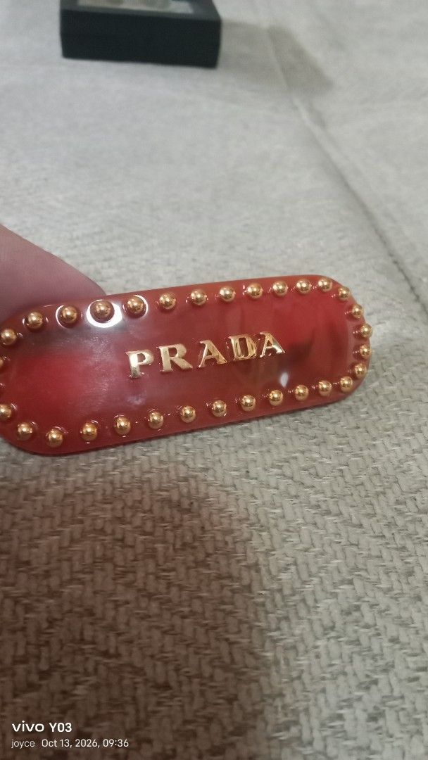 Prada Red Hair Clip with Gold Studs (Category: Hair Accessories) located in Cabuyao City. Submitted by selections888 (Listing ID 1467612809, Image 3). Description: - Brand: Prada - Material: Premium red acetate with gold-tone hardware - Design: Gold-tone metal studs along the border with raised gold Prada lettering on the front - Hardware: Gold-tone clasp closure stamped with 'PRADA' and 'MADE IN ITALY' - Inclusions: Comes with the original black