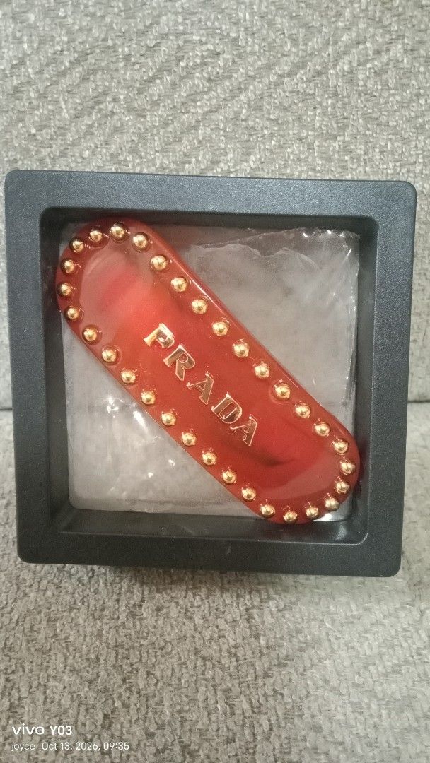 Prada Red Hair Clip with Gold Studs (Category: Hair Accessories) located in Cabuyao City. Submitted by selections888 (Listing ID 1467612809, Image 1). Description: - Brand: Prada - Material: Premium red acetate with gold-tone hardware - Design: Gold-tone metal studs along the border with raised gold Prada lettering on the front - Hardware: Gold-tone clasp closure stamped with 'PRADA' and 'MADE IN ITALY' - Inclusions: Comes with the original black