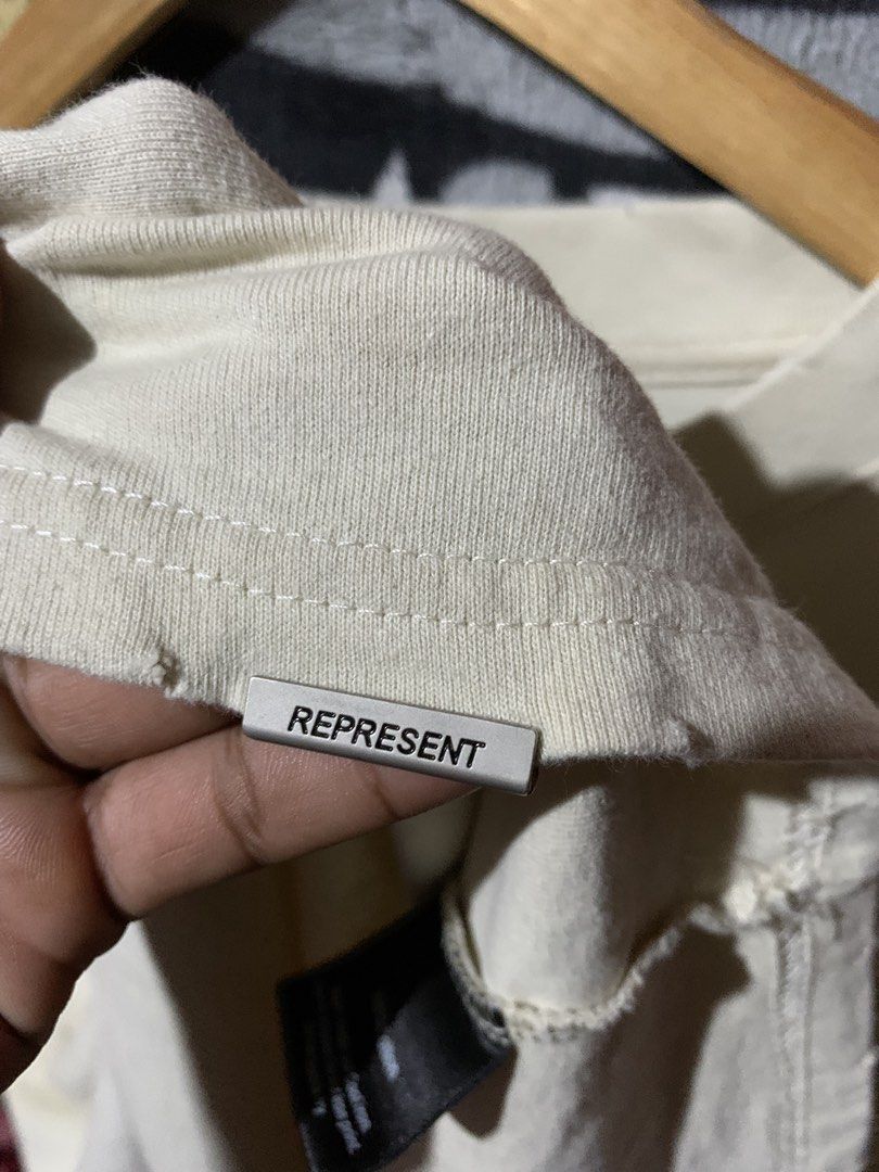 Represent Shark Only The Strong Survive Tee (Category: Tshirts & Polo Shirts ) located in Tayug. Submitted by cvcthrift (Listing ID 1467805723, Image 3). Description: 24/30 NO ISSUE EXCELLENT CR-9.5/10 - Brand: Represent - Color: Cream - Size: Medium - Material: 100% cotton - Design: Front shark graphic with 'Only The Strong Survive' text in red - Details: Distressed collar and signature metal Represent tag near the hem - Condition: Includes inne