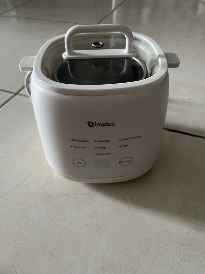 Simplus Multi-Function Egg Boiler and Steamer (Category: Cookers) located in Kuala Lumpur. Submitted by adamdrakebundle (Listing ID 1467627601, Image 1). Description: - Brand: Simplus - Functions: Cook eggs, make yogurt, and steam food - Design: White body, clear glass lid, inner stainless steel bowl, and plastic steam rack insert - Controls: Digital touch panel with multiple timer settings (soft-boiled, steam, boil) - Condition: Used a few times