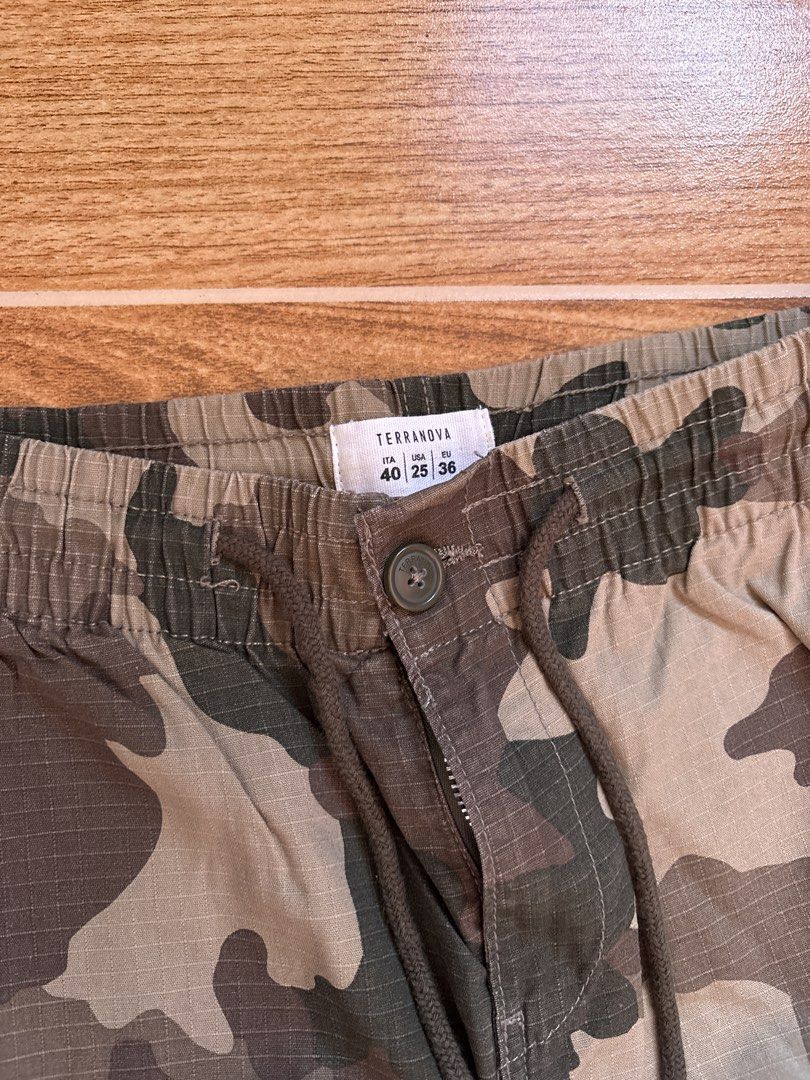 Terranova Camouflage Cargo Pants (Category: Jeans) located in Manila. Submitted by _foryou (Listing ID 1467672628, Image 3). Description: - Brand: Terranova - Design: Camouflage in green, brown, and tan tones - Size: ITA 40, USA 25, EU 36 - Material: Durable ripstop fabric - Waist: Elastic waistband with drawstring, button closure, and zip fly - Pockets: Functional cargo pockets on both thighs and back pockets with button flaps - Hem: Adjustable 