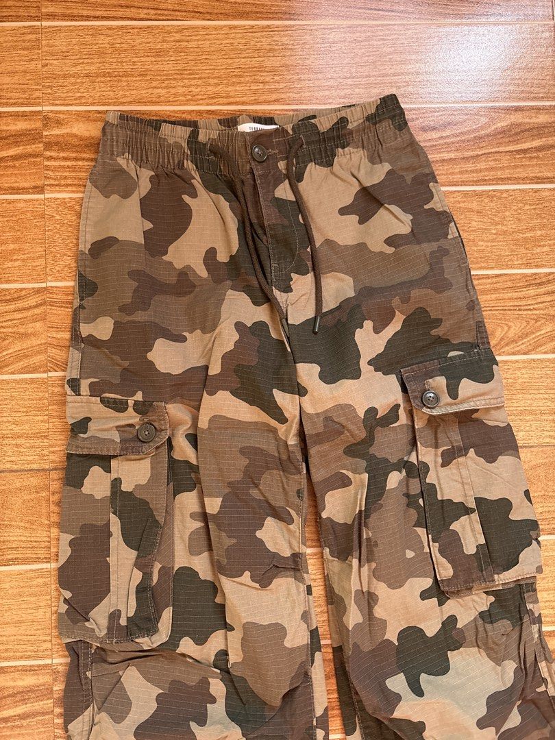 Terranova Camouflage Cargo Pants (Category: Jeans) located in Manila. Submitted by _foryou (Listing ID 1467672628, Image 2). Description: - Brand: Terranova - Design: Camouflage in green, brown, and tan tones - Size: ITA 40, USA 25, EU 36 - Material: Durable ripstop fabric - Waist: Elastic waistband with drawstring, button closure, and zip fly - Pockets: Functional cargo pockets on both thighs and back pockets with button flaps - Hem: Adjustable 