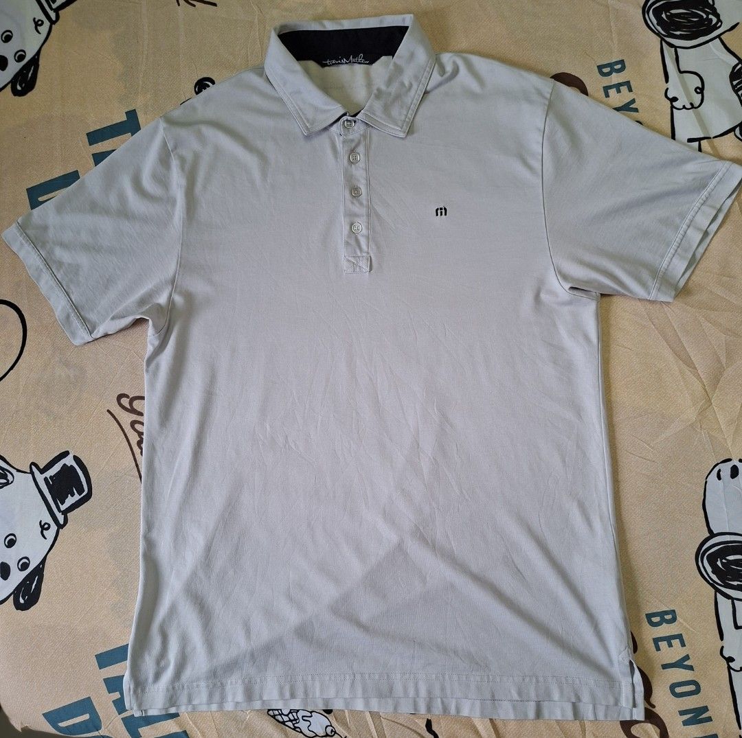 Travis Mathew Four Button Placket Golf Polo Shirt (Category: Activewear) located in Rizal. Submitted by carou66859 (Listing ID 1467619421, Image 1). Description: This is a light gray short-sleeve polo shirt from Travis Mathew featuring a four-button placket and a small embroidered "m" logo on the chest.Size 21 inches width and 29 inches length.The retail price for a new TravisMathew polo shirt typically ranges between $89.95 and $109.95 when purc