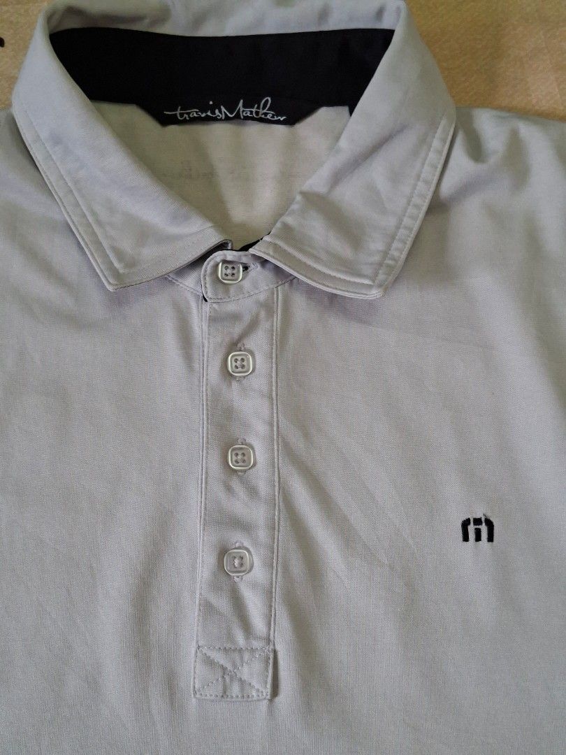 Travis Mathew Four Button Placket Golf Polo Shirt (Category: Activewear) located in Rizal. Submitted by carou66859 (Listing ID 1467619421, Image 2). Description: This is a light gray short-sleeve polo shirt from Travis Mathew featuring a four-button placket and a small embroidered "m" logo on the chest.Size 21 inches width and 29 inches length.The retail price for a new TravisMathew polo shirt typically ranges between $89.95 and $109.95 when purc
