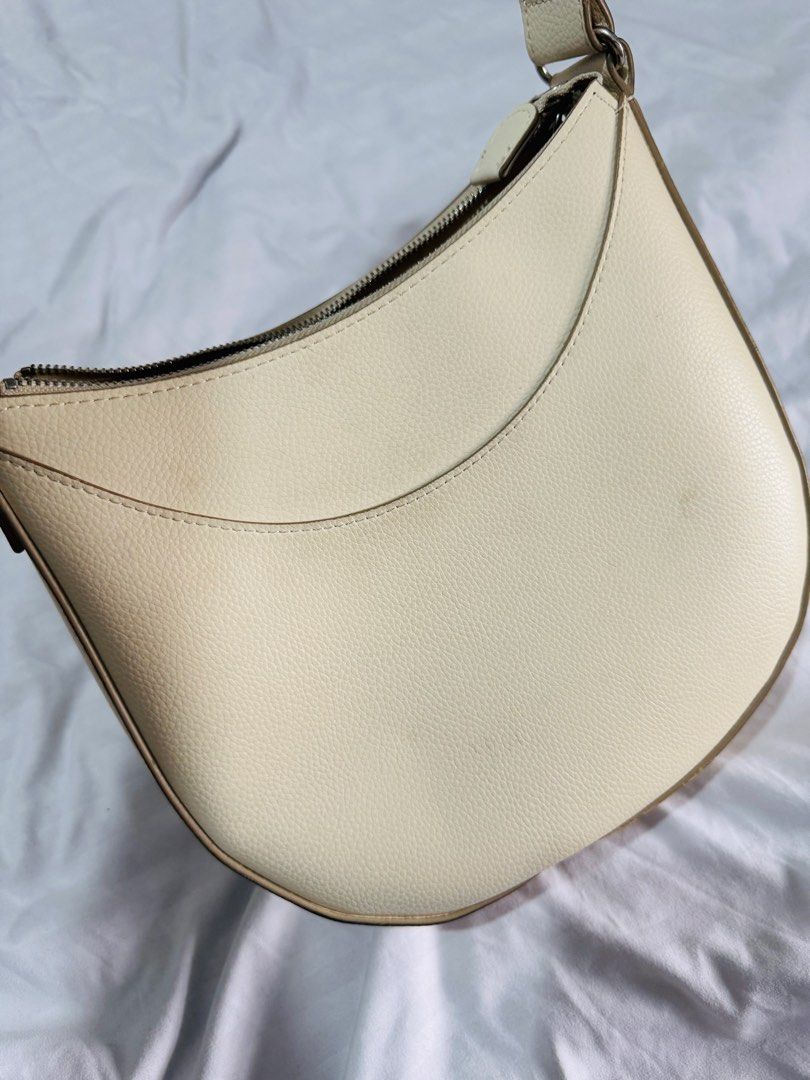 Uniqlo Shoulder bag with adjustable strap- BEIGE (Category: Shoulder Bags) located in Pasig City. Submitted by marizanne04 (Listing ID 1467667349, Image 2). Description: - Color: Off-white - Material: Textured faux leather with matching fabric lining - Design: Structured half-moon shape with clean lines - Hardware: Silver-tone hardware - Closure: Secure zip top closure - Compartments: Two interior slip pockets - Strap: Matching adjustable shoulde